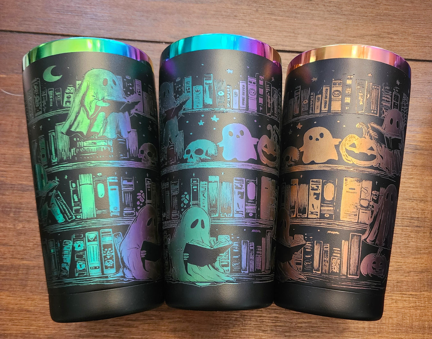 Three tumbler cups with Halloween-themed designs on a wooden surface
